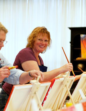 Woman paints the edges of her canvas at a Come Paint With Us class